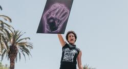 Black woman at a protest, holding up a sign of a neon black fist