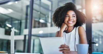 Black woman smiling and looking out window with laptop