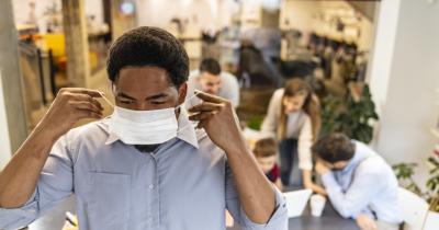 Black worker putting on mask with people waiting in the background