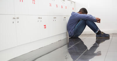 Black College Student Sitting on the Classroom Floor Looking Down in Despair