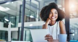 Black woman smiling and looking out window with laptop