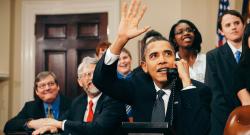 President Obama on the phone waving surrounded by staffers
