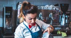 Working-class barista pouring steamed milk into a cup