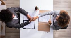 Two people shaking hands across a table in an interview