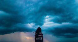 View of woman from behind as she looks out at incoming storm clouds