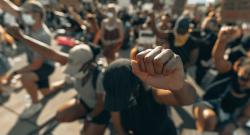 Black, brown, and white protestors knee with their heads down and their fists in the air