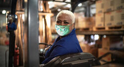 Black warehouse worker wearing mask operating forklift