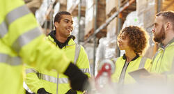 Diverse group of warehouse workers meeting among the warehouse shelves.