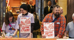 A group of people is standing together in an indoor setting, holding signs that read, "We have the resources to make everything we love resilient." The signs also feature the logos for MN350 and 100 Percent Campaign. 