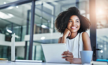 Black woman smiling and looking out window with laptop