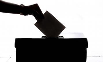 Backlit hand dropping vote into ballot box