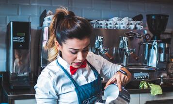 Working-class barista pouring steamed milk into a cup