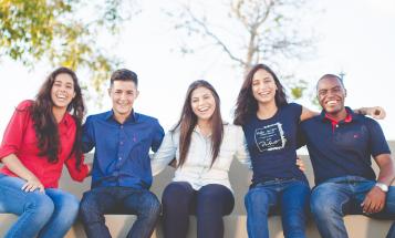 Group of smiling college students sitting outside on a bench