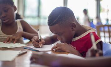 Young Black student writing on paper in school