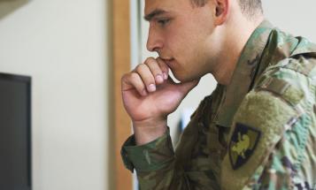 A young off-duty soldier looking contemplatively at a computer.
