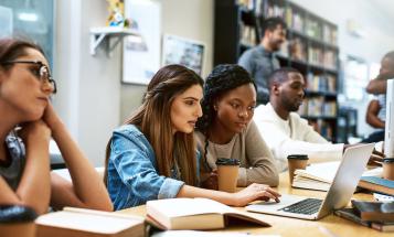 Two college students working together on laptop in library