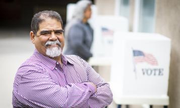 Smiling Latino man in front of voting booths
