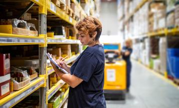 Woman warehouse worker holding clipboard, surveying inventory