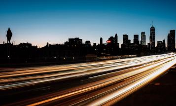 Blur of traffic light in front of backlit Manhattan skyline