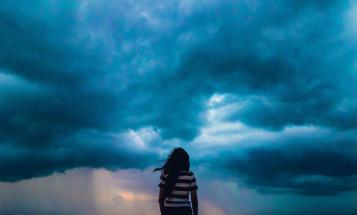 View of woman from behind as she looks out at incoming storm clouds