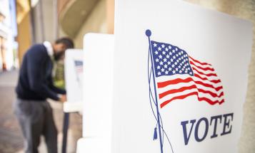 Black voter at a distance in a voting booth with an empty booth in the foreground