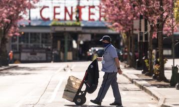 Masked postman pushing dolly on empty street