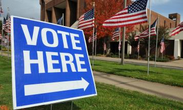 "Vote Here" sign in the grass in front of a polling station