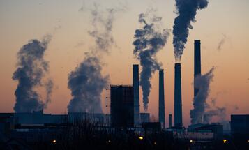 Backlit view of a factory at sunset with smoke spilling from smokestacks