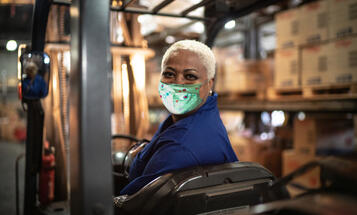 Black warehouse worker wearing mask operating forklift