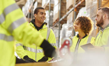 Diverse group of warehouse workers meeting among the warehouse shelves.