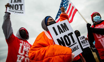 For Us Not Amazon action involving Black organizers dressed for cold weather, carrying 'I am not disposable' signs and carrying an American flag.