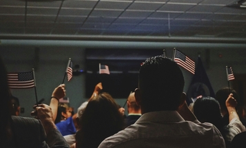 A depiction of a naturalization ceremony including a group of individuals waving flags