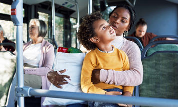 A woman and young child ride a city bus with a bag of groceries.