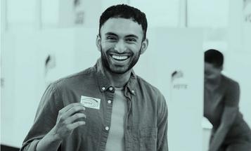 Man smiling holding an I Voted sticker at a polling station.