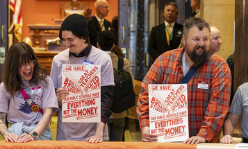 A group of people is standing together in an indoor setting, holding signs that read, "We have the resources to make everything we love resilient." The signs also feature the logos for MN350 and 100 Percent Campaign. 