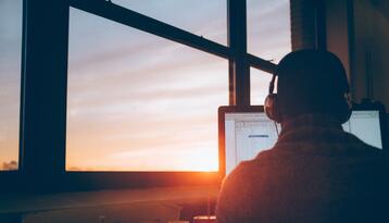 Backlit person wearing headphones facing computer