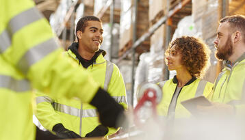 Diverse group of warehouse workers meeting among the warehouse shelves.