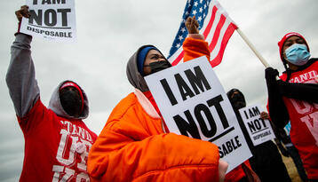 For Us Not Amazon action involving Black organizers dressed for cold weather, carrying 'I am not disposable' signs and carrying an American flag.