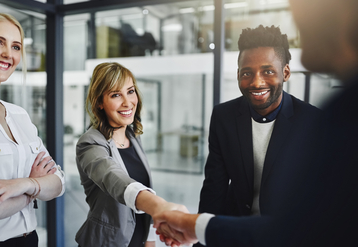 Smiling white woman and Black man shaking the hand of a job applicant