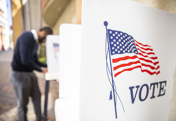 Black voter at a distance in a voting booth with an empty booth in the foreground