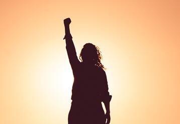 Person backlit by the setting sun with their fist raised in the air