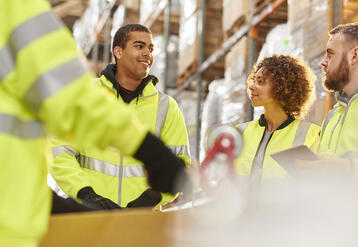 Diverse group of warehouse workers meeting among the warehouse shelves.