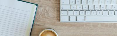 Notebook, headphones, keyboard and cup of coffee from overhead