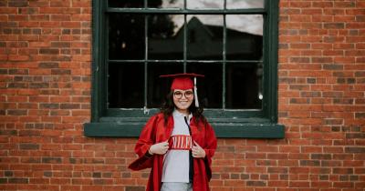 Young female college graduate in red cape and hat outside