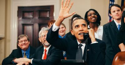 President Obama on the phone waving surrounded by staffers