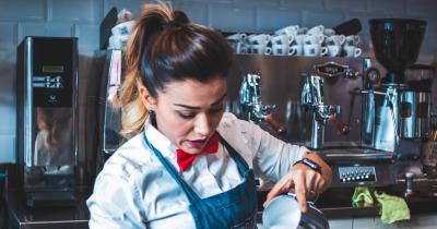 Working-class barista pouring steamed milk into a cup