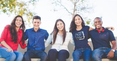 Group of smiling college students sitting outside on a bench
