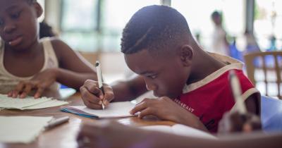 Young Black student writing on paper in school