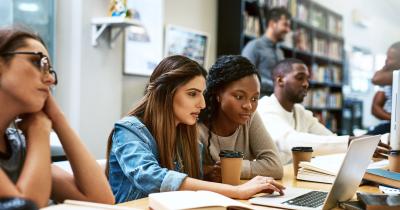 Two college students working together on laptop in library