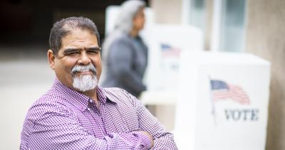 Smiling Latino man in front of voting booths